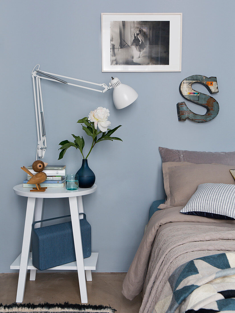Nachttisch mit Leselampe neben Bett im Schlafzimmer mit blau-grauer Wand