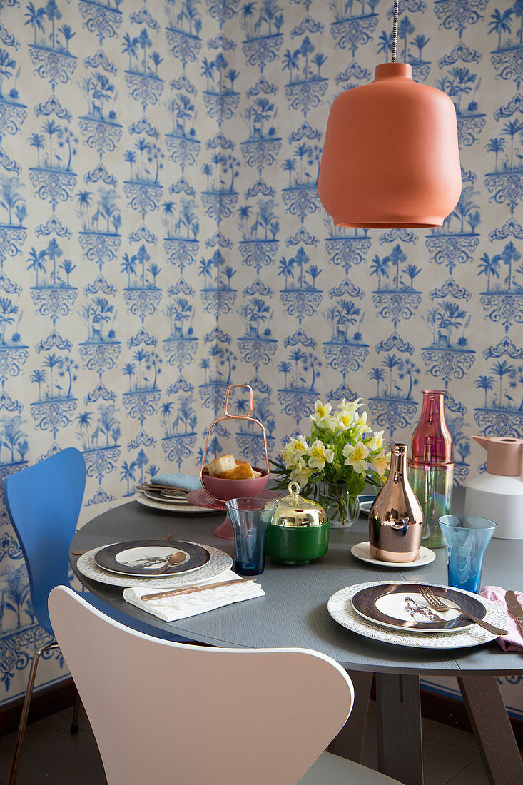 Gedeckter runder Tisch mit Designerstühlen vor blau-weißer Tapete