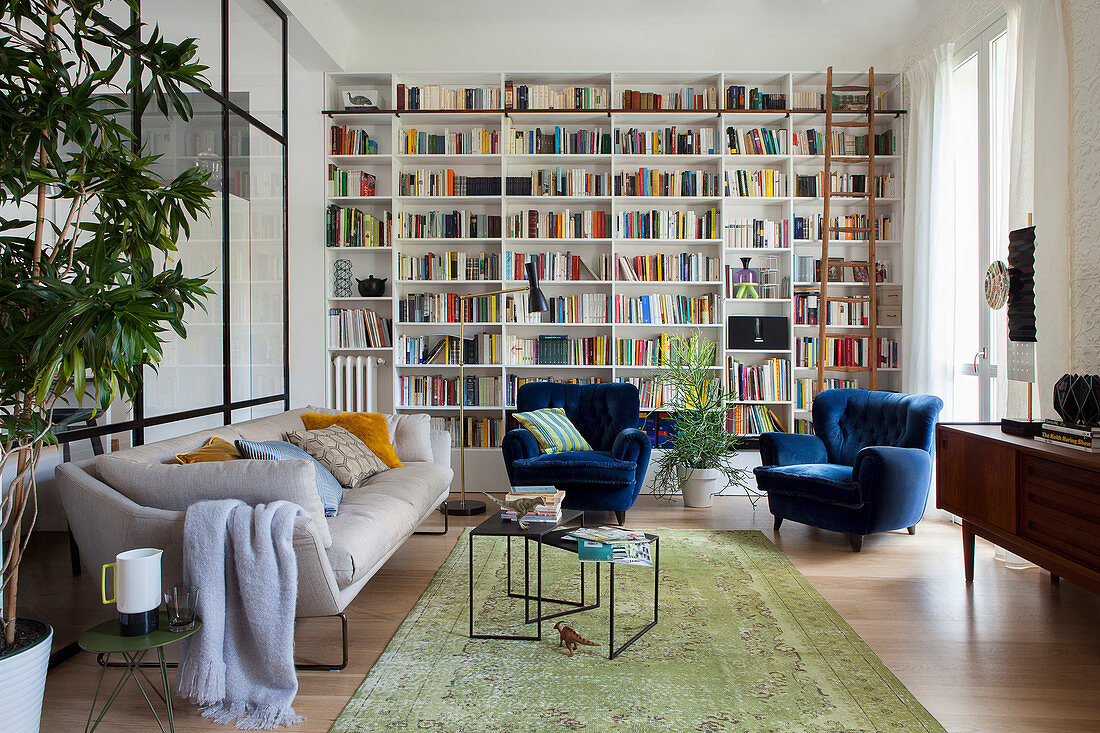 Wohnzimmer im Stilmix mit deckenhoher Bücherwand, Sofa und blauen Samtsesseln