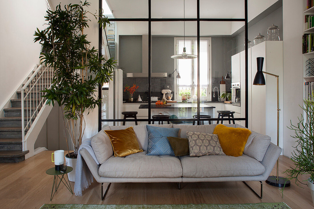 Blick vom Wohnbereich mit Sofa in die Küche abgetrennt durch raumhohe Glaswand