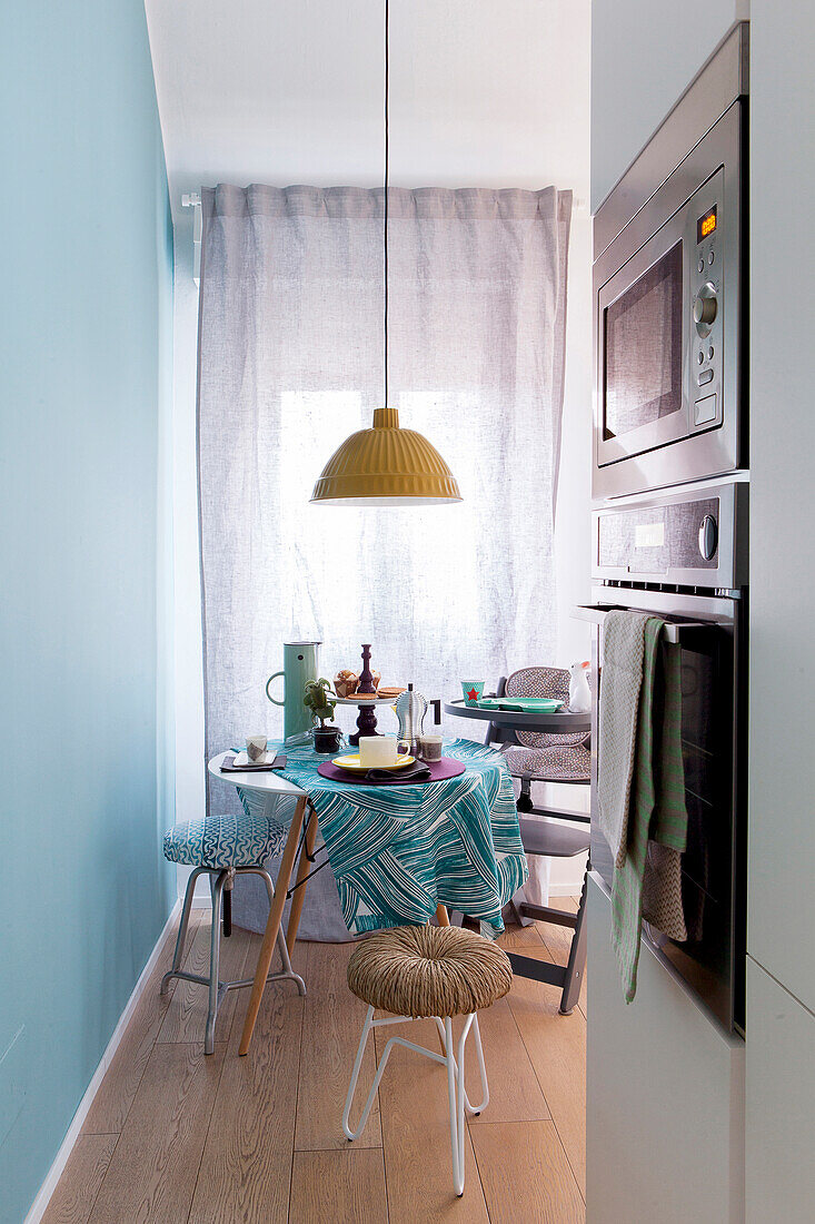 Fitted appliances in kitchen with round table with turquoise tablecloth in background