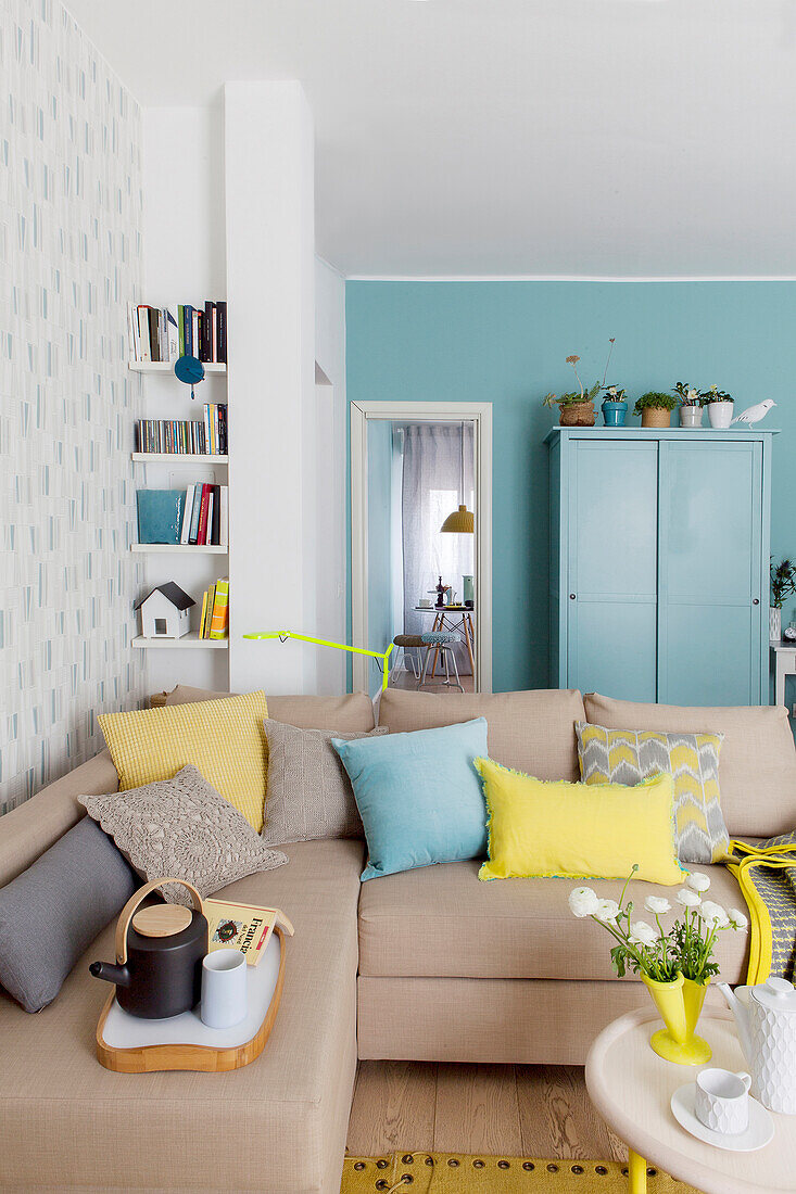 Beige corner sofa in front of blue cupboard against blue wall