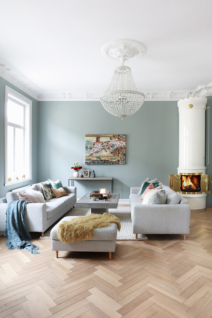Sofa set, coffee table and Swedish tiled stove in living room with herringbone parquet floor