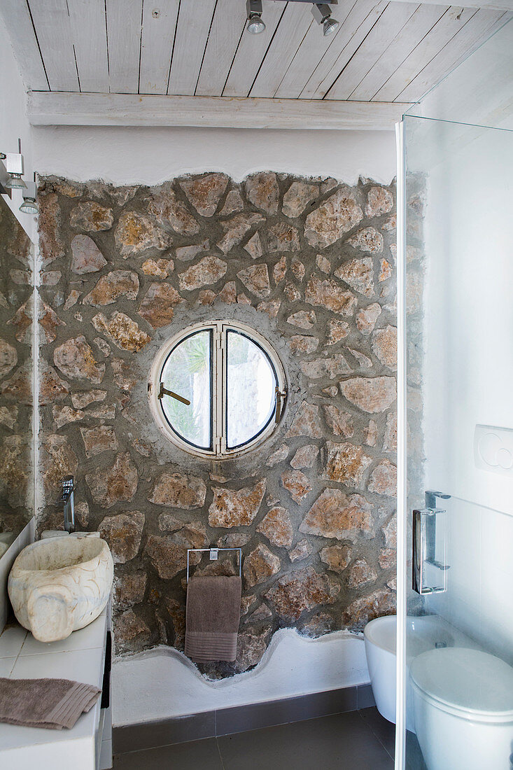 Round window in stone wall of small bathroom