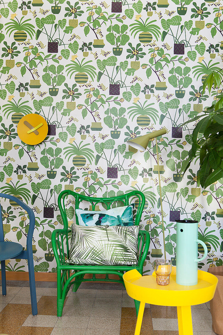 Green chair and yellow side table in reading area against wallpaper with plant motifs