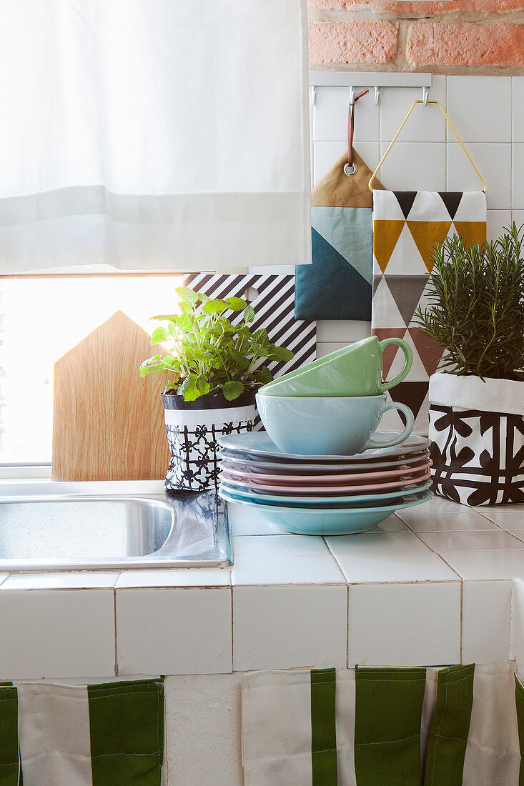 Crockery and potted herbs on white-tiled kitchen surface