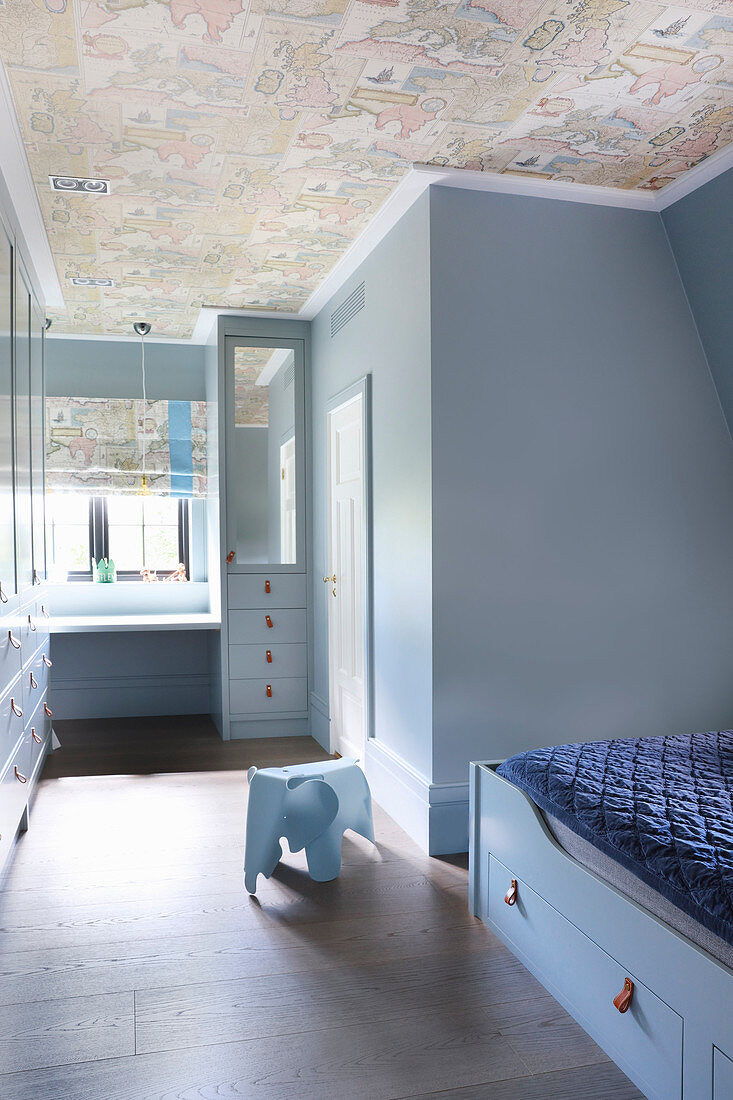 Boy's room decorated entirely in pale blue with vintage-effect wallpaper on ceiling