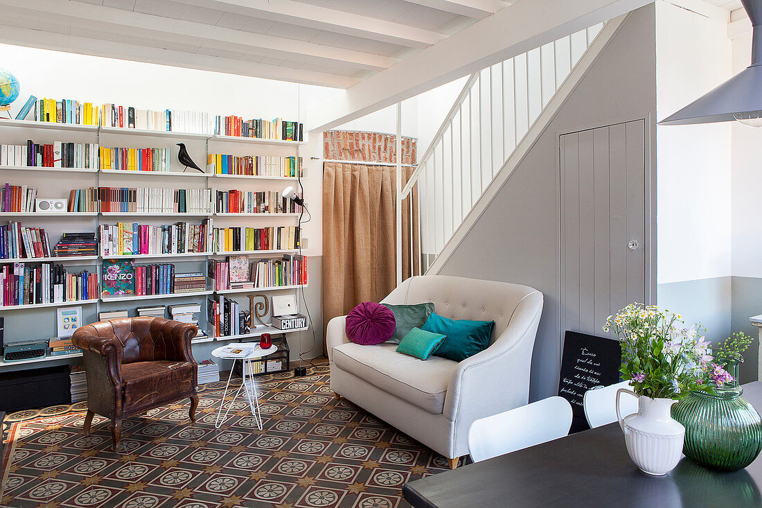 Bücherwand, alter Ledersessel, Beistelltisch und Sofa vor Treppenwand im Wohnzimmer