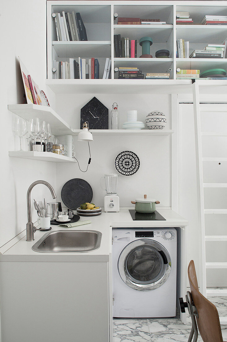 Kleine Küche und Waschmaschine, darüber Regal im Einzimmer-Apartment