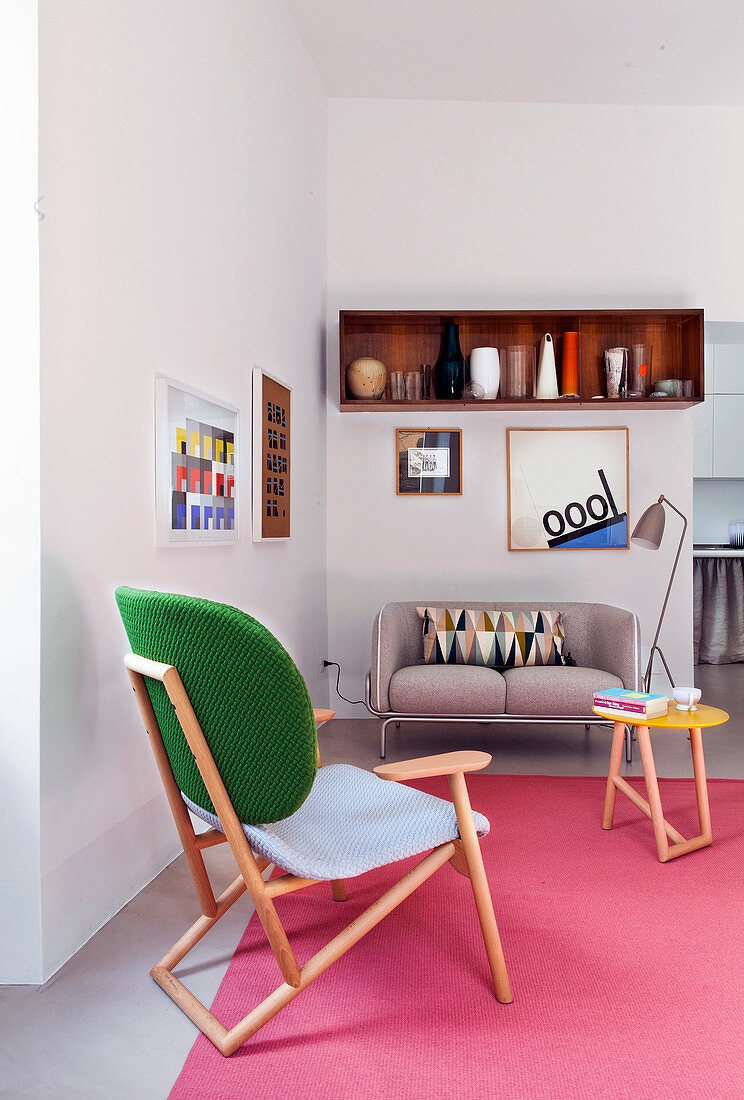 Sitzecke mit Sofa, Holzstuhl und rosafarbenem Teppich in kleinem Apartment
