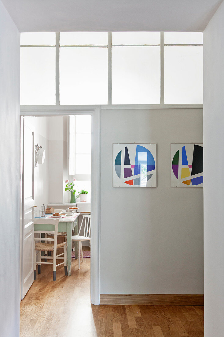 Modern abstract artworks on hallway wall next to doorway leading into vintage-style kitchen