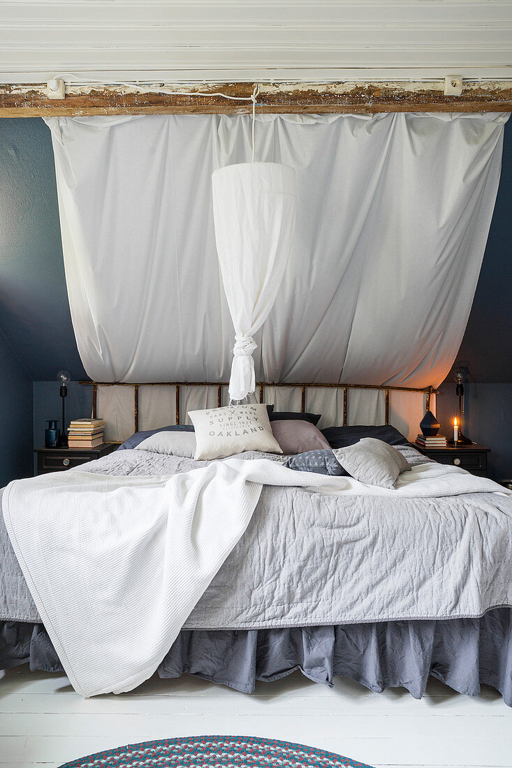 Grey and white double bed with ruffles and DIY canopy under sloping ceiling