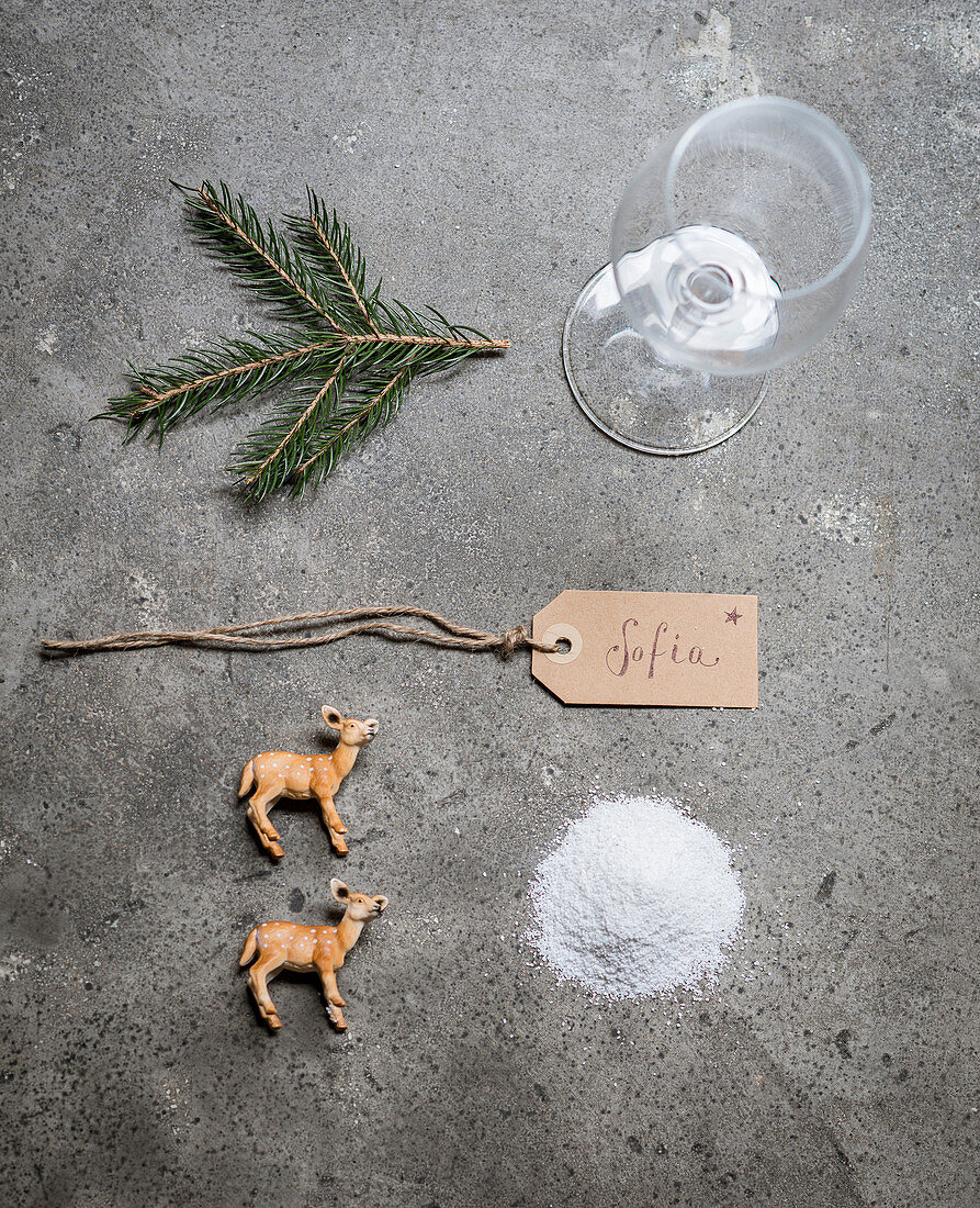 Wine glass, pine twig, name tag, deer figurines and salt for making a winter-landscape place card