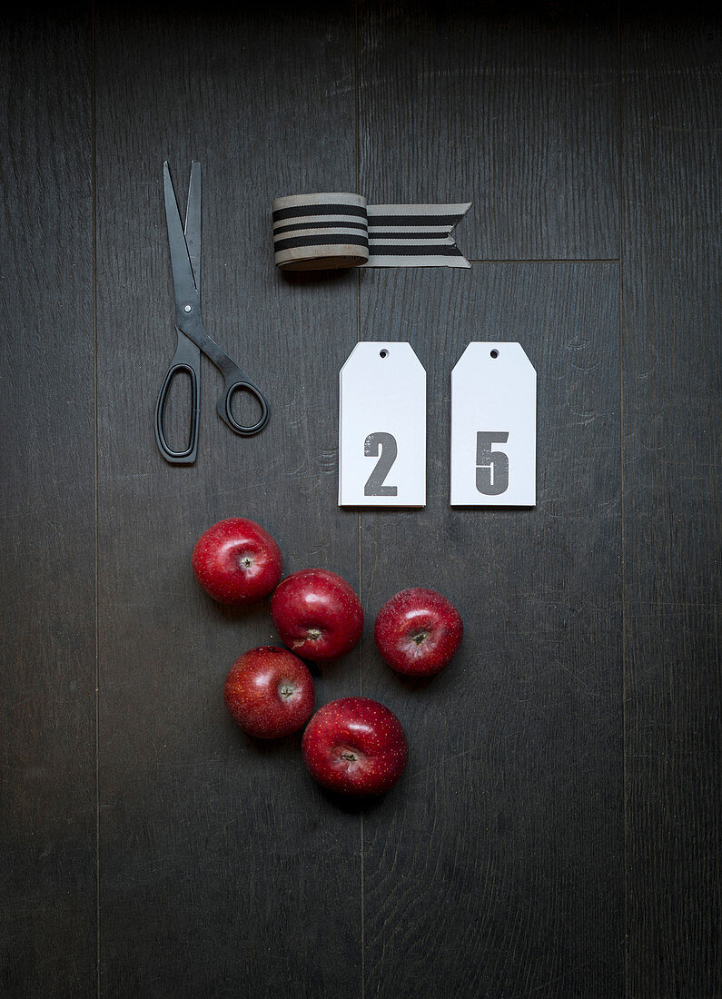 Dekoband, Kärtchen mit Zahlen, rote Äpfel und Schere auf dunklem Untergrund