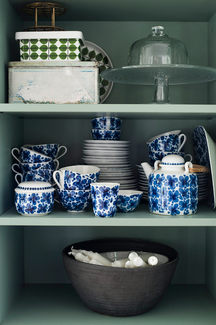 Crockery with blue floral pattern and bowl of candles in cupboard