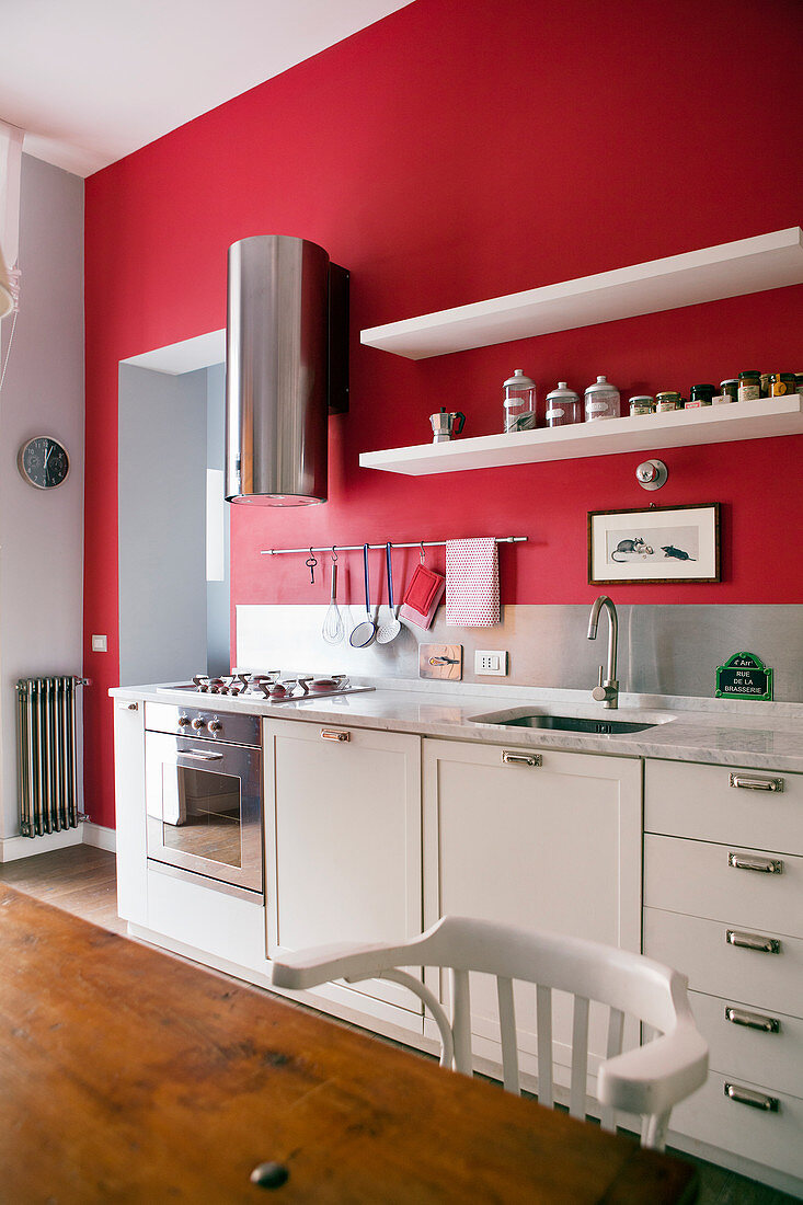 Weiße Küchenzeile mit moderner Edelstahlabzugshaube vor rot gestrichener Wand
