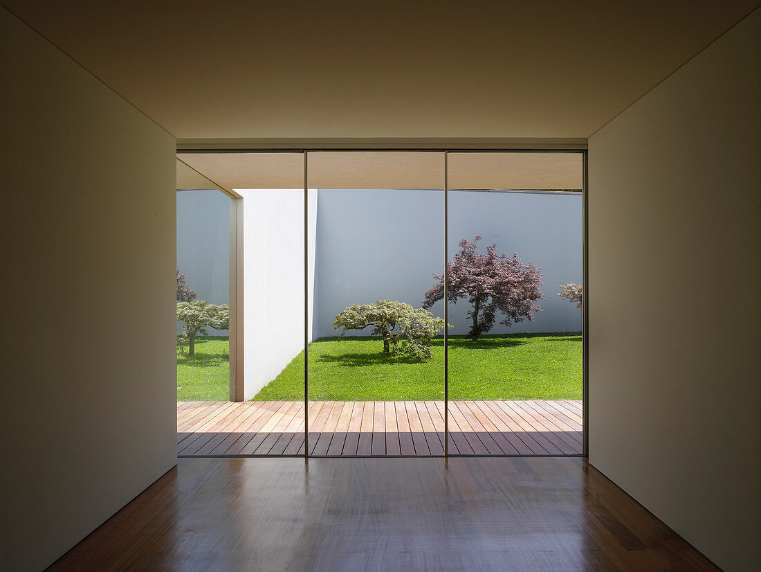 View from cubist, minimalist interior through glass wall onto wooden terrace and courtyard garden