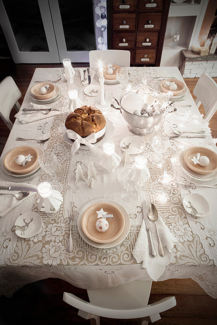 Blick von Oben auf weihnachtlich gedeckten Tisch in Weiß mit Spitzendecke und Teelichtern