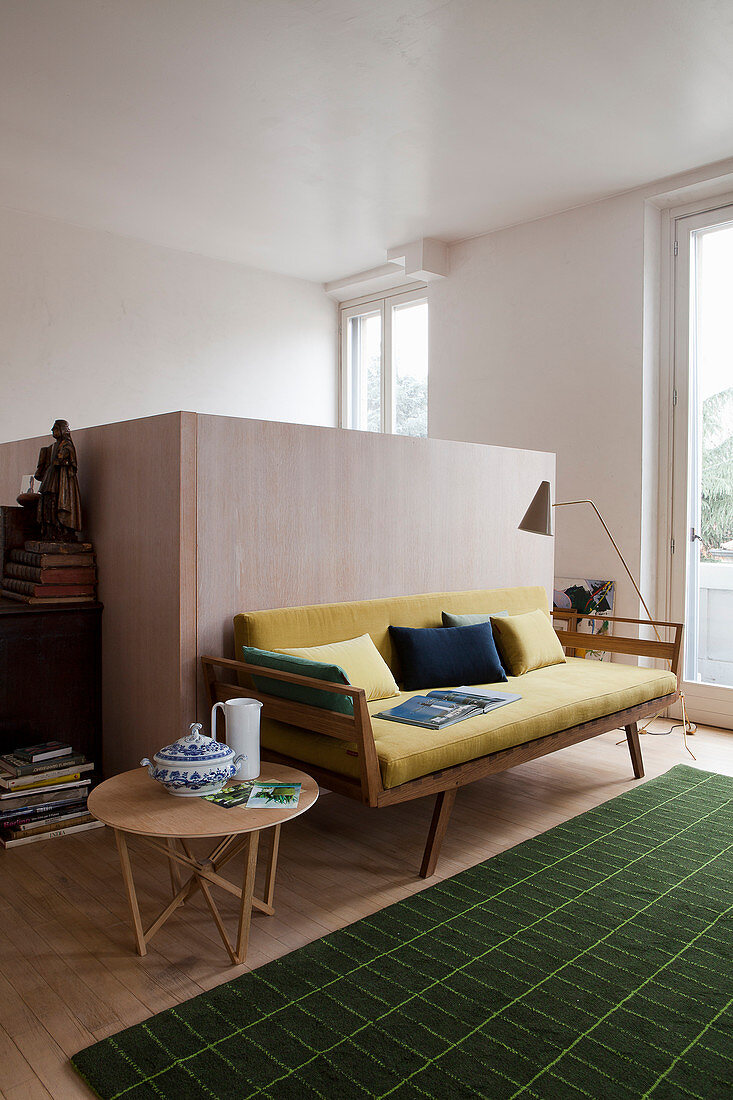 Yellow retro sofa, side table and green rug in front of half-height wooden partition