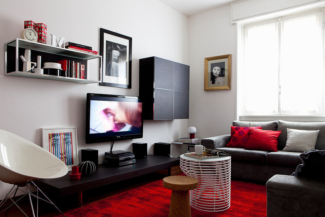 Wohnzimmer mit schwarzen Möbeln und roten Farbakzenten durch Teppich und Kissen
