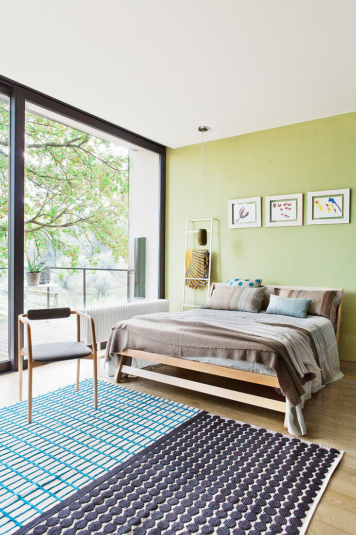 Light-flooded bedroom with glass wall and wooden bed against pastel green wall