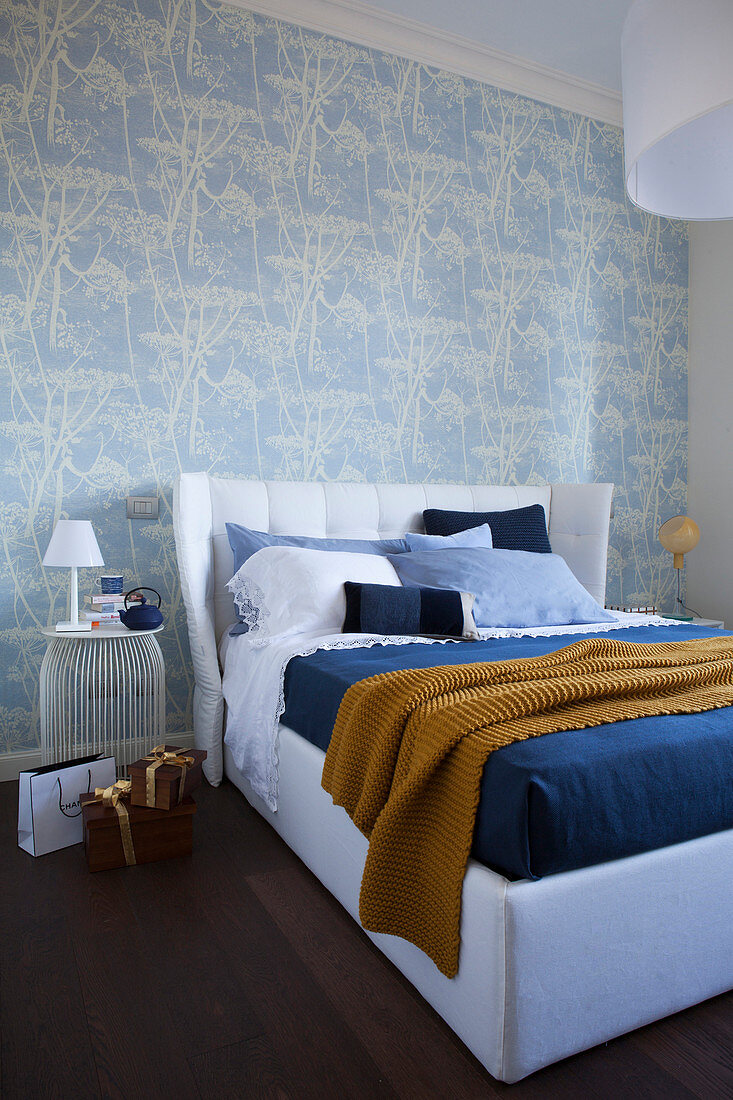 Double bed with upholstered headboard against blue-and-white patterned wallpaper in bedroom