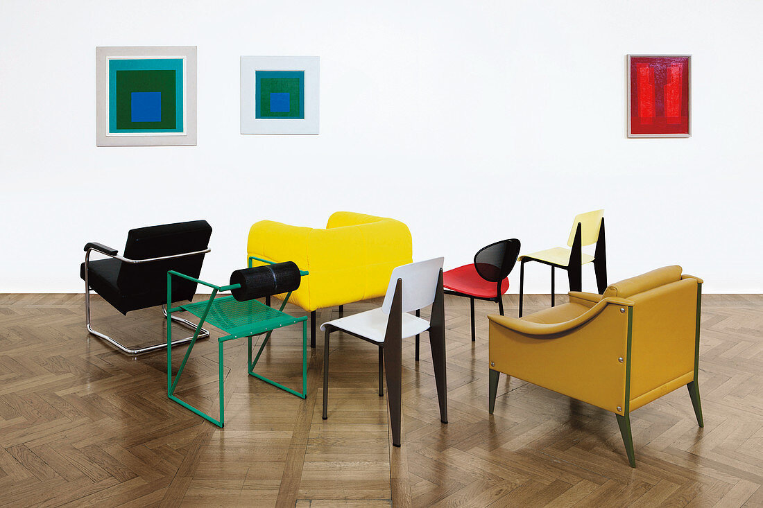 Verschiedene Designerstühle vor Wand mit abstrakten Kunstwerken
