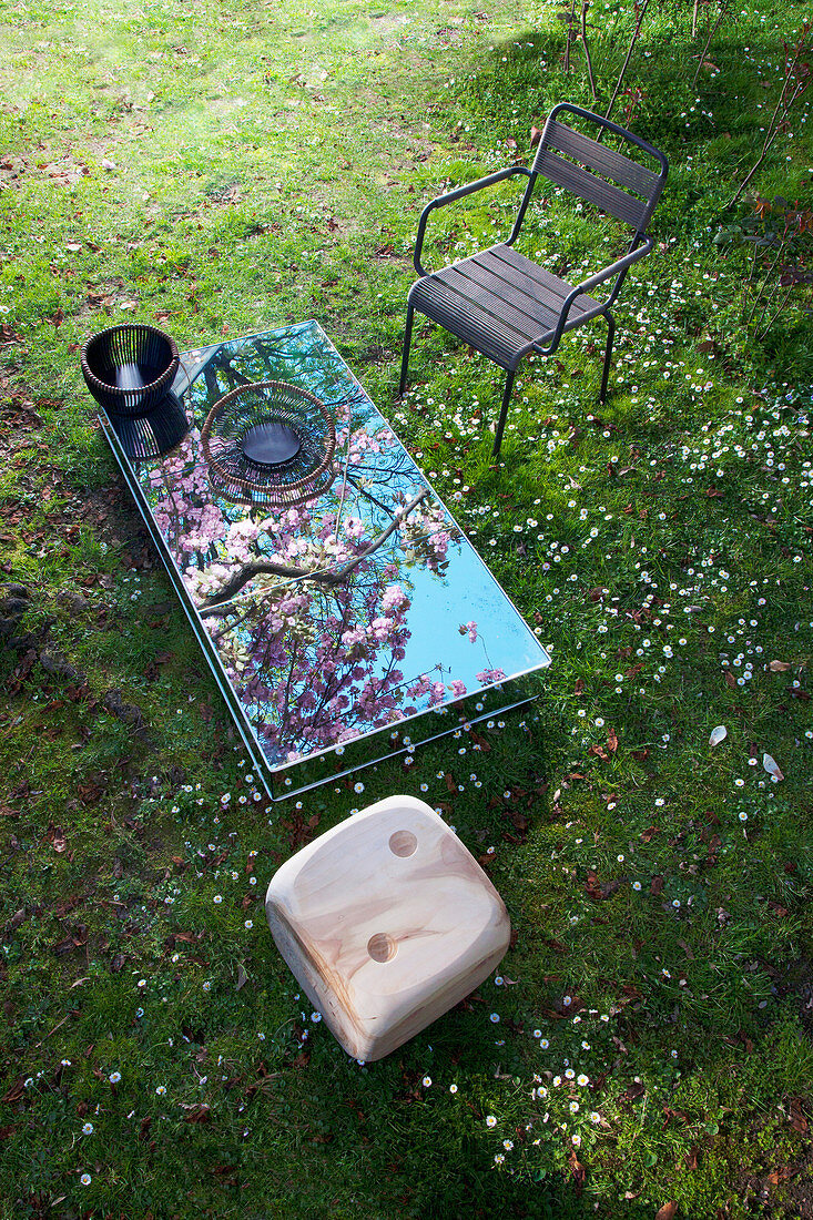 Spiegelglastisch, Armlehnstuhl und Zedernhocker in Würfelform auf Frühlingswiese