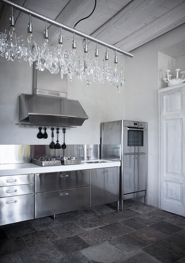 Stainless steel kitchen counter, tiled floor and modern chandelier in country house
