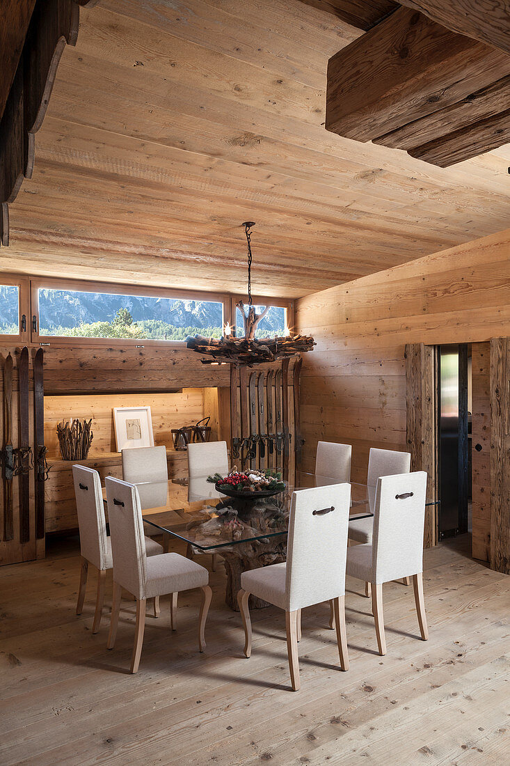 Chairs with white upholstery around glass dining table in rustic wooden house
