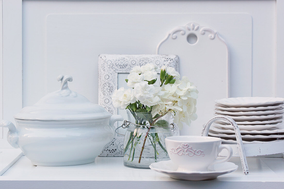 Vase of white carnations and hydrangeas and china crockery on dresser