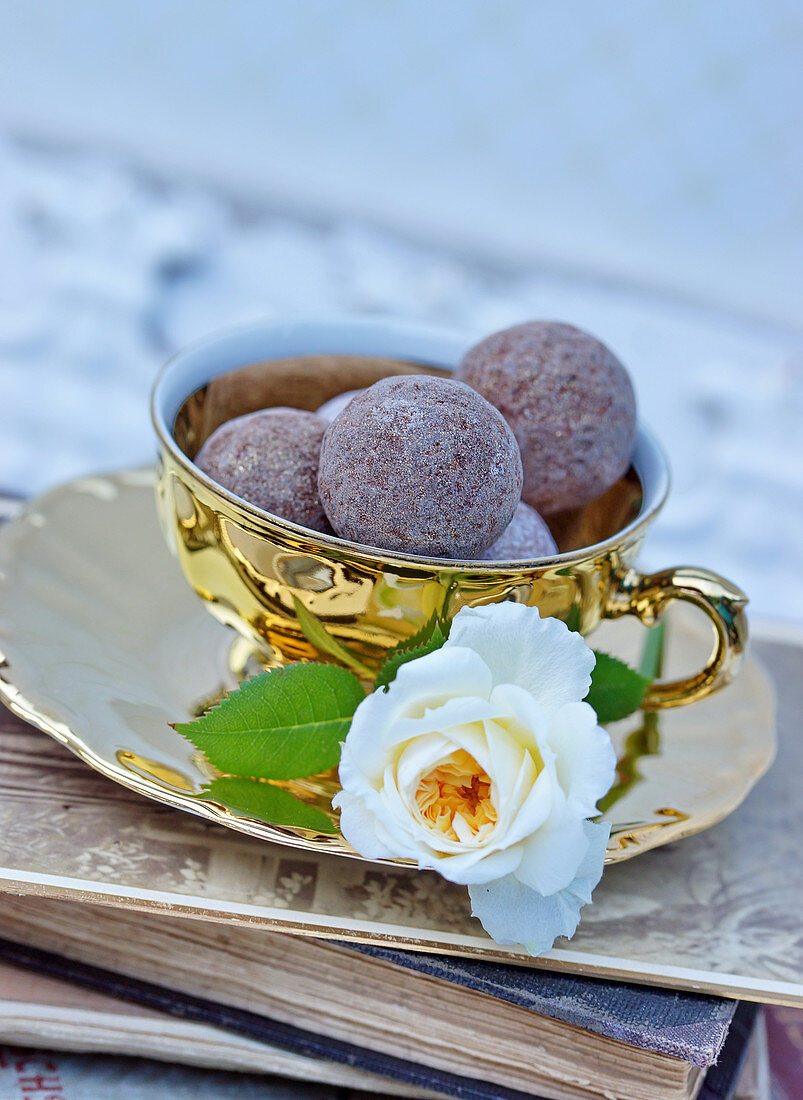 Goldene Kaffeetasse mit Pralinen und Rosenblüten