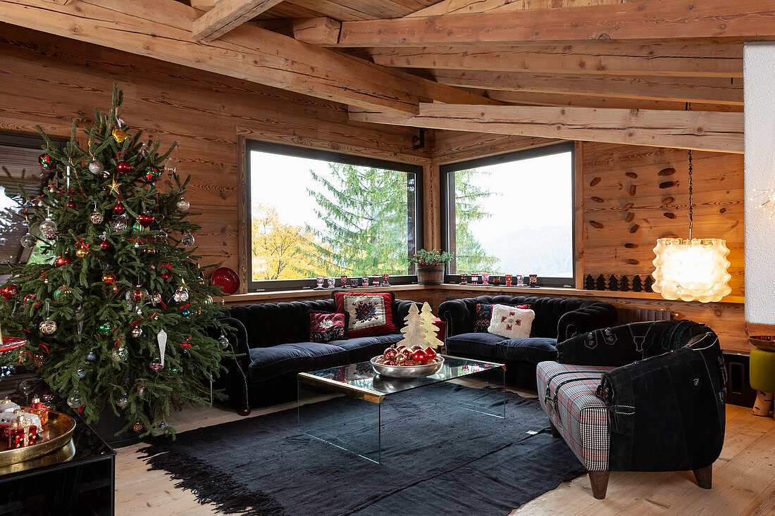 Geschmückter Weihnachtsbaum und schwarze Polstermöbel im Wohnzimmer eines Chalets