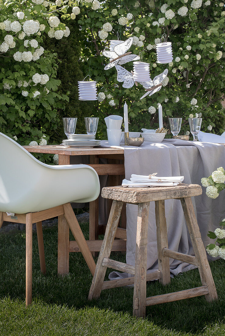 Table set in white and beige in garden in front of viburnum bush
