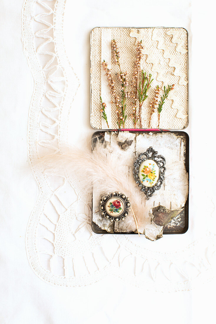 Old tin decorated with birch bark, brooches, feather, sprigs of heather and fabric