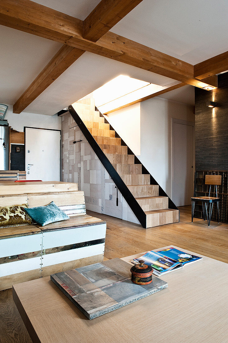 Wohnraum mit Sitzbank, Couch und Treppenaufgang aus recycelten Materialien