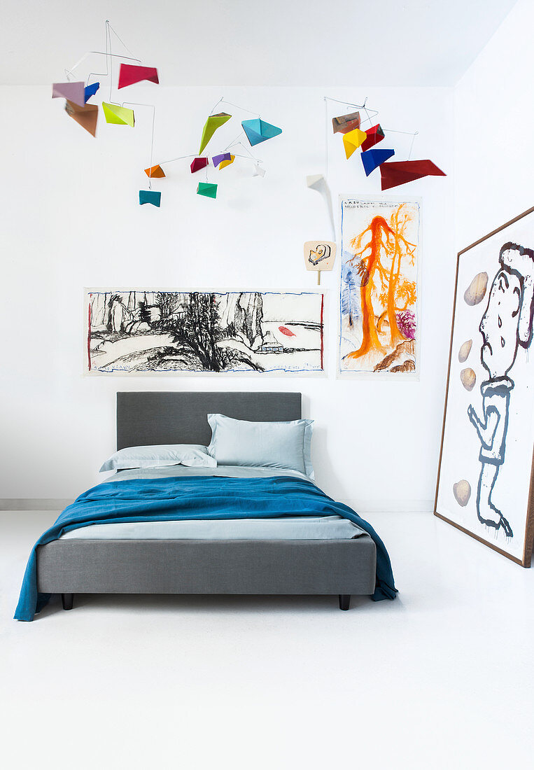 Graues Bett in Zimmerecke dekoriert mit modernen Wandbildern