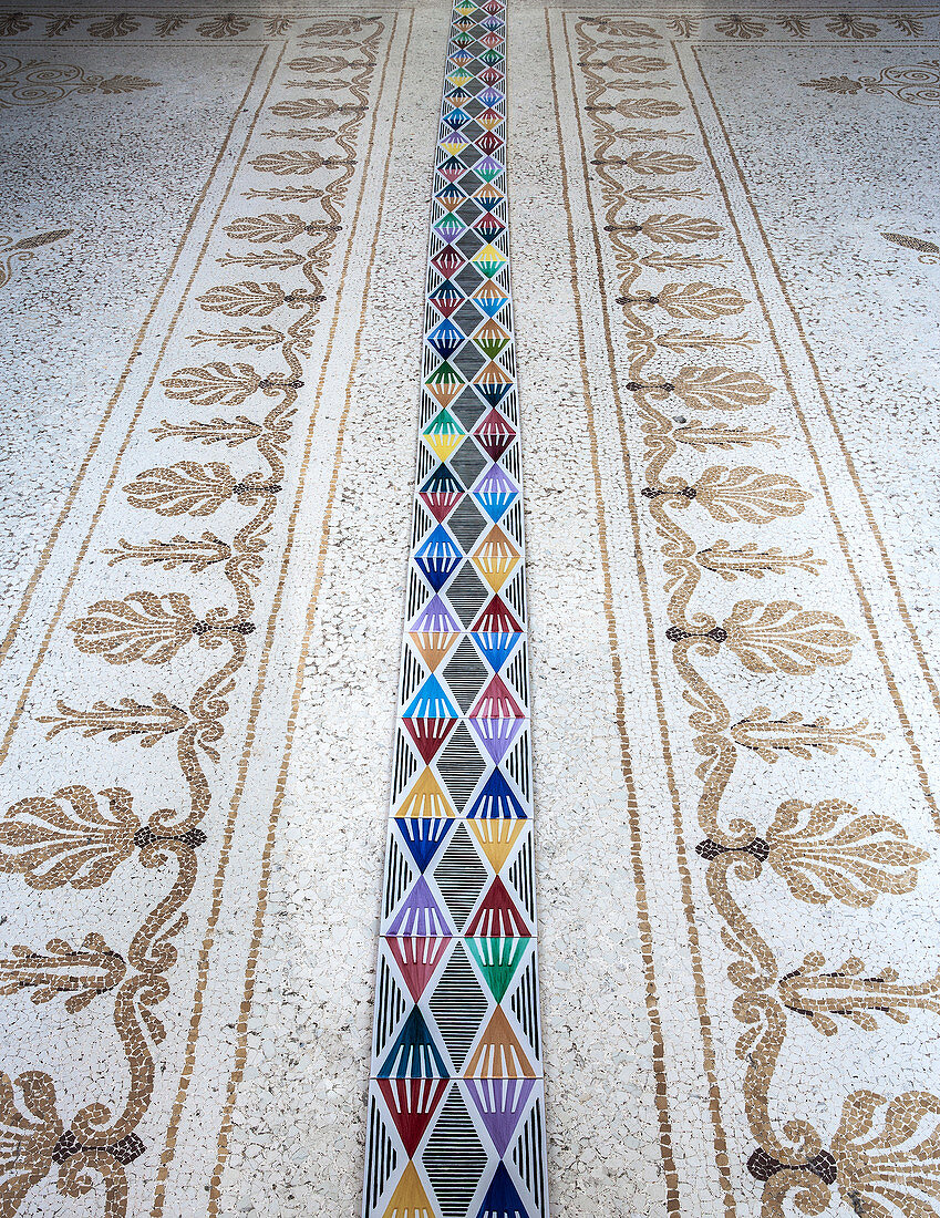 Strip of modern, multicoloured, geometric tiles on antique mosaic floor