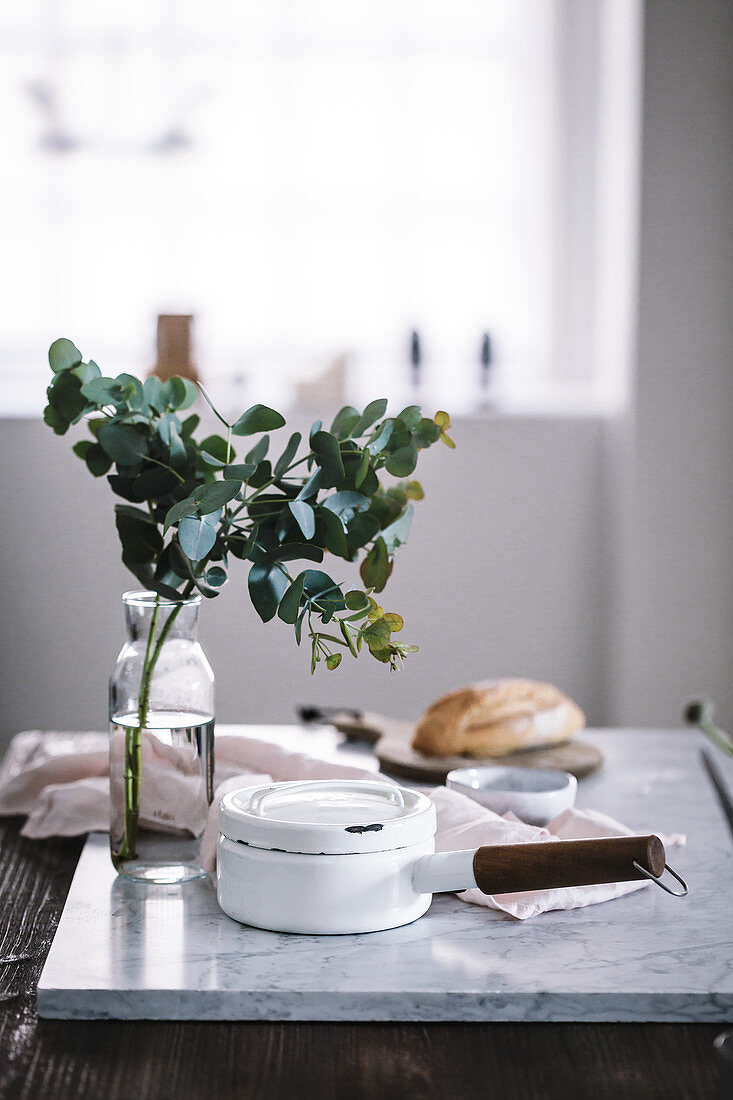Eukalyptuszweige in Vase neben Emailletopf auf Marmorplatte in Küche