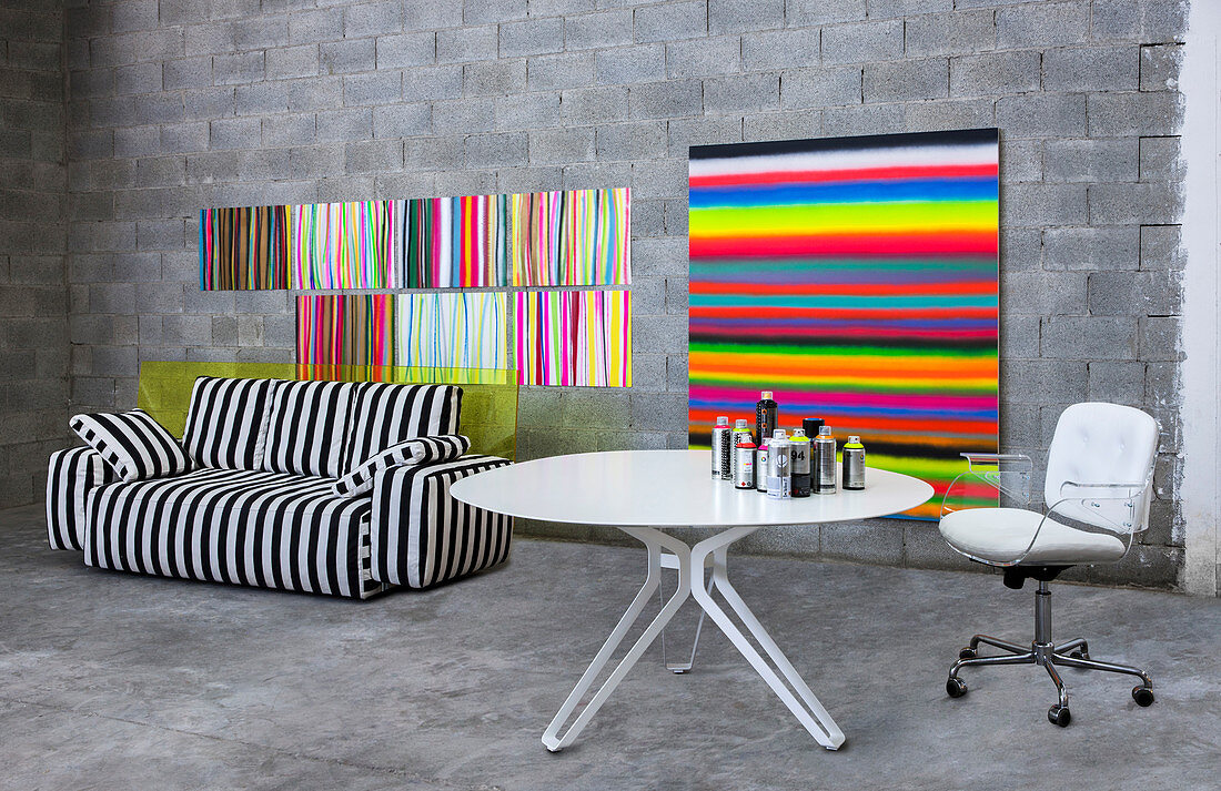 Swivel chair at round table next to monochrome striped sofa and multicoloured striped artworks