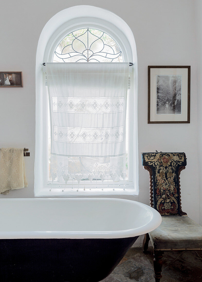 Nostalgisches Bad mit besticktem Antikstuhl und Spitzengardine vor Rundbogenfenster