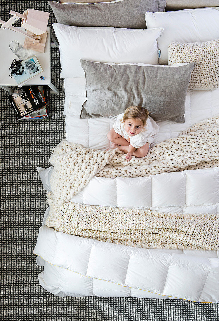 Mädchen auf dem Bett mit Strickdecken und Kissen in Naturtönen