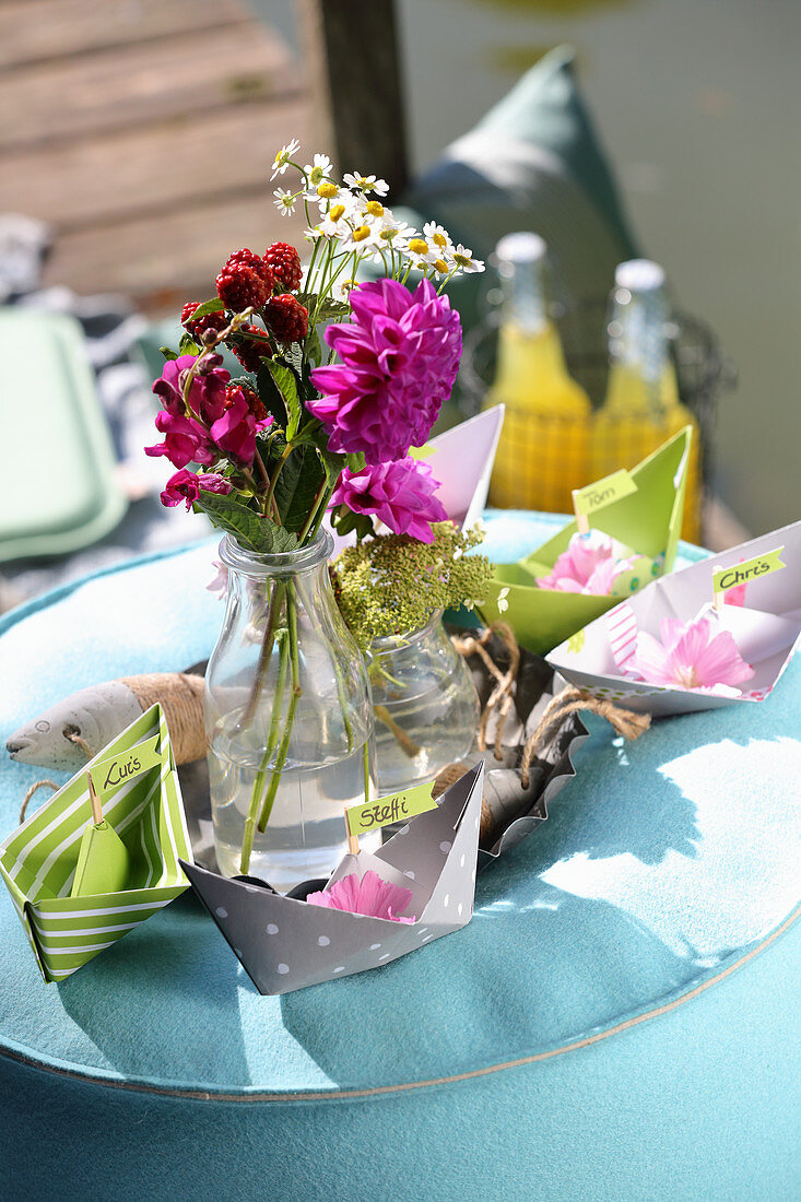 Paper boats and garden flowers as decoration for picnic on lake