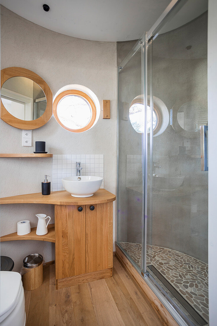 Wooden washstand and glass shower doors in bathroom in round extension of tiny house