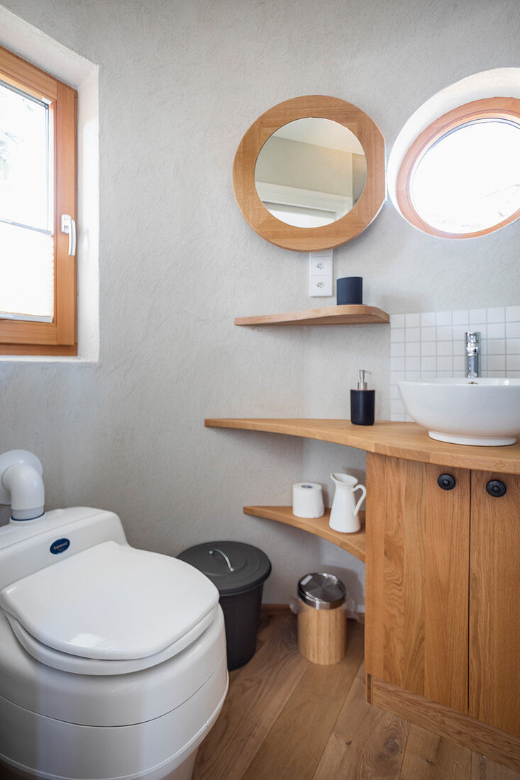 Wooden washstand, porthole window and toilet in bathroom of tiny house