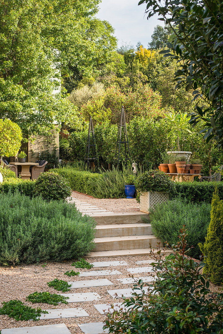 Kiesweg mit Steinplatten und Treppe in üppig bepflanzter Gartenanlage