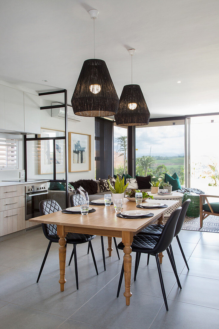 Black pendant lamps above dining table with turned legs in open-plan interior
