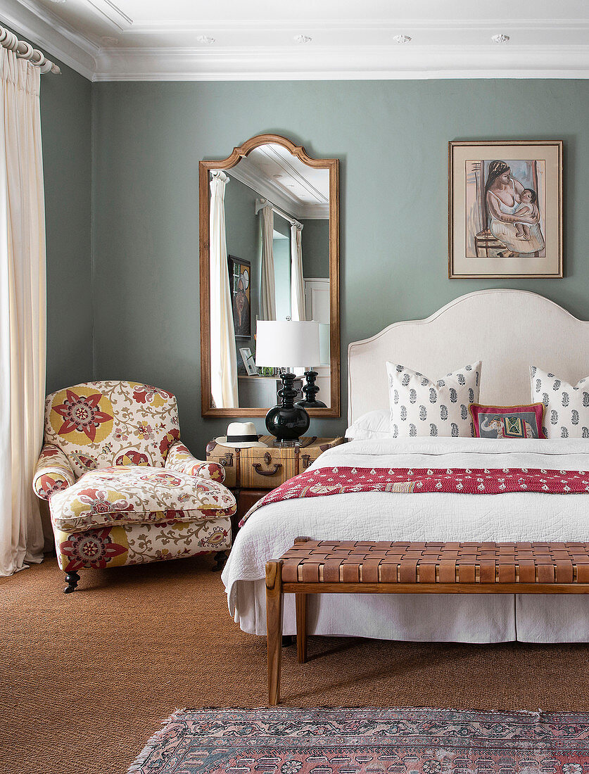 Bench at foot of bench and armchair with floral upholstery in romantic, elegant bedroom