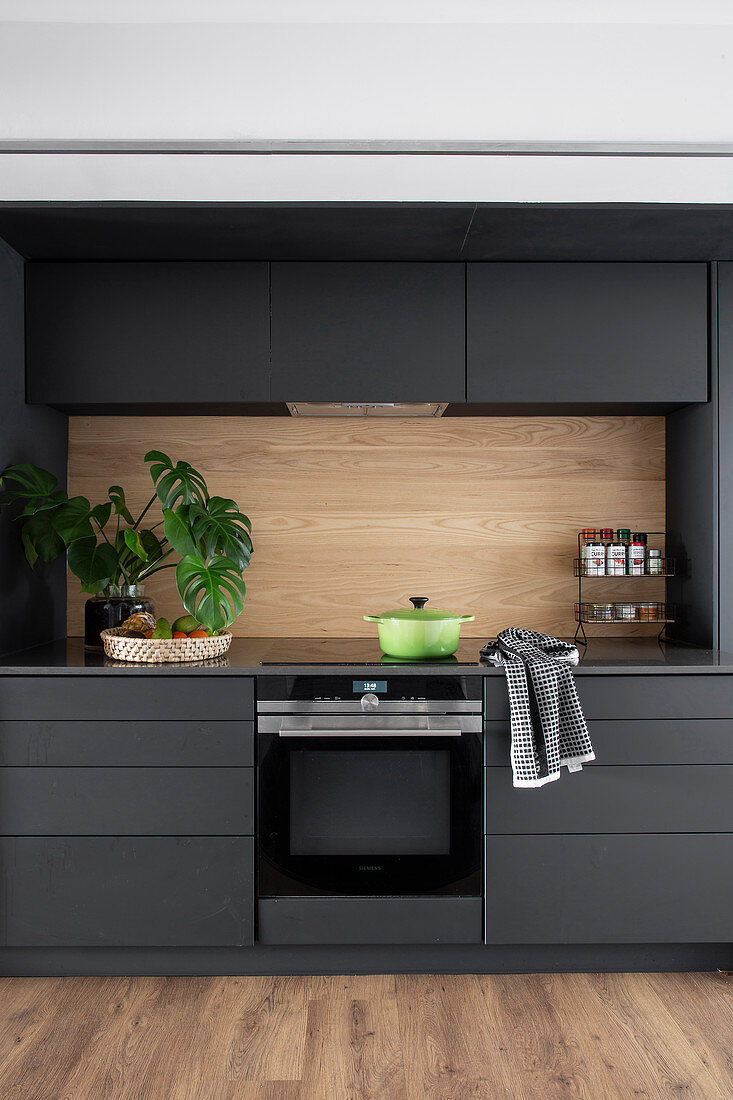 Anthrazitfarbene Küche mit Oberschränken und Holz-Rückwand