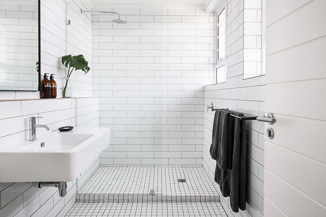 Badzimmer mit weißen Metrofliesen und rahmenloser Glastrennwand zur Dusche